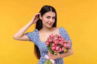 Photo of Happy young woman with beautiful bouquet on orange background