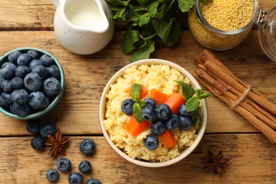 Photo of Tasty millet porridge with blueberries, pumpkin and mint in bowl on wooden table, flat lay