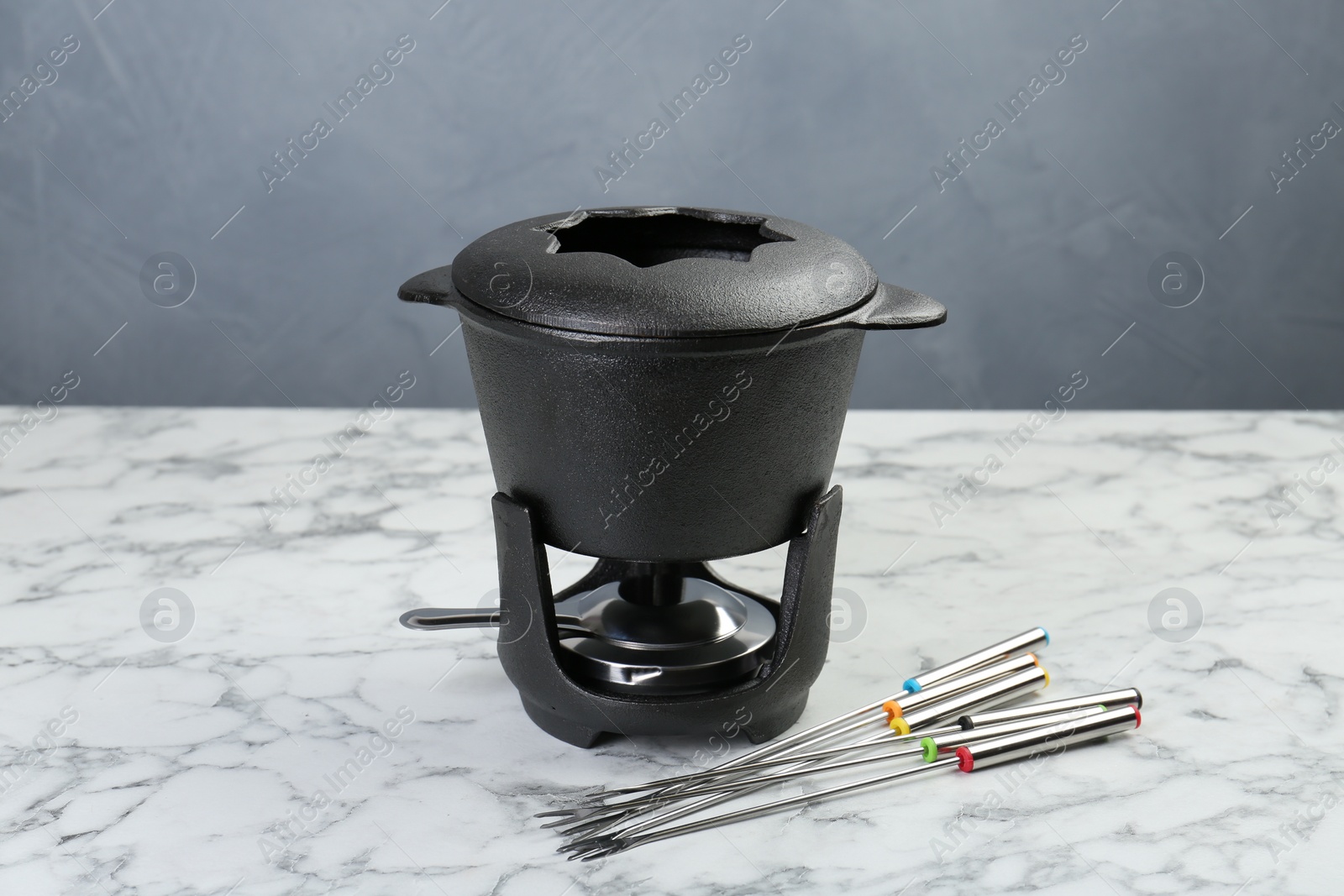 Photo of Fondue set on white marble table against grey background