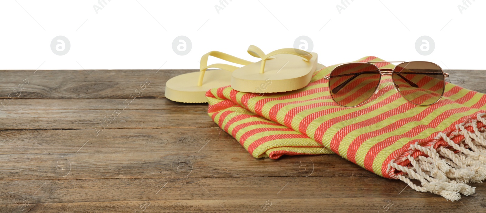 Photo of Beach towel, flip flops and sunglasses on wooden surface against white background. Space for text