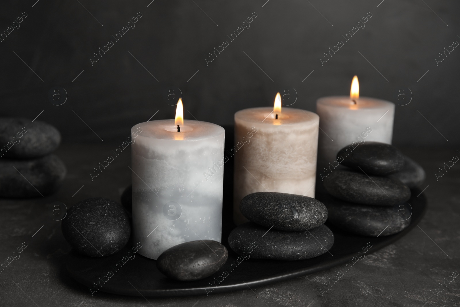 Photo of Burning candles and spa stones on grey table