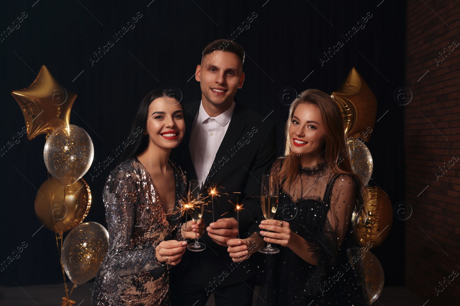 Photo of Happy friends with glasses of sparkling wine and sparklers celebrating New Year indoors