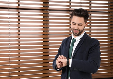 Portrait of confident businessman checking time at window indoors. Space for text