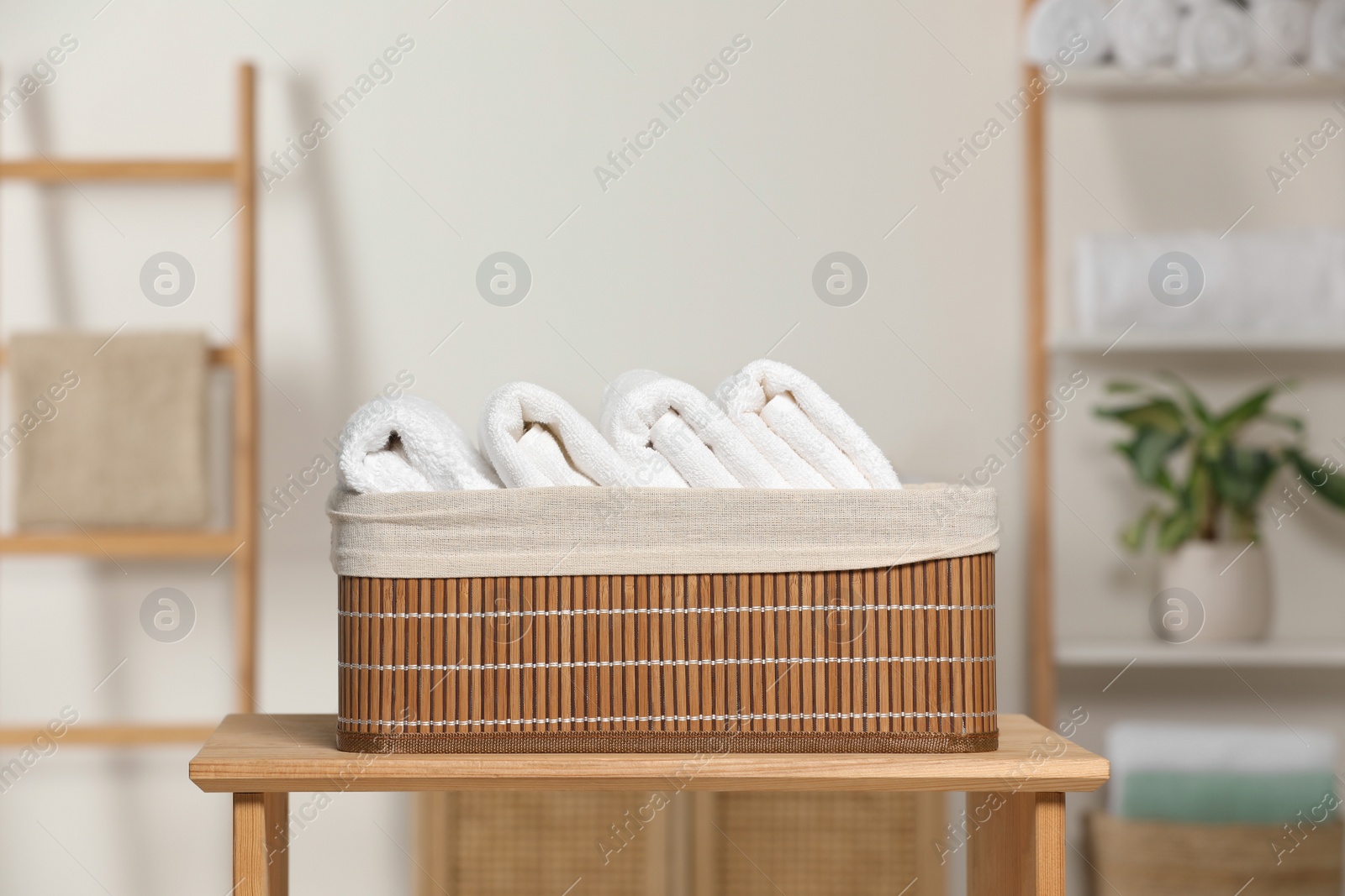 Photo of Wicker basket with folded soft terry towels on wooden table indoors