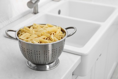 Photo of Cooked pasta in metal colander on countertop near sink. Space for text
