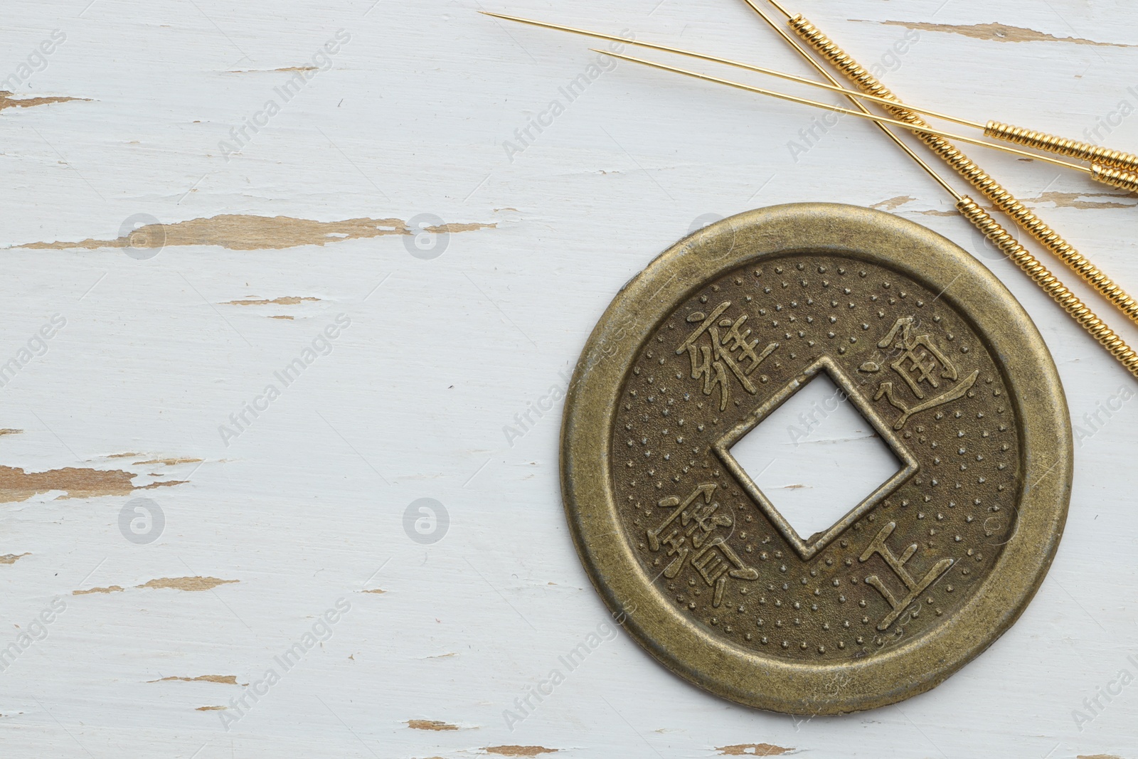 Photo of Acupuncture needles and Chinese coin on white wooden table, flat lay. Space for text