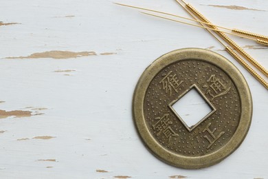 Photo of Acupuncture needles and Chinese coin on white wooden table, flat lay. Space for text