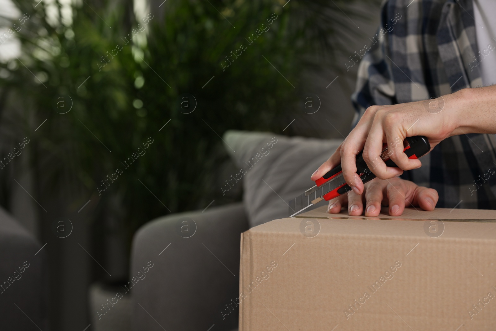 Photo of Man using utility knife to open parcel at home, closeup. Space for text