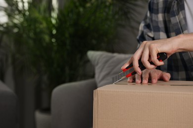 Photo of Man using utility knife to open parcel at home, closeup. Space for text