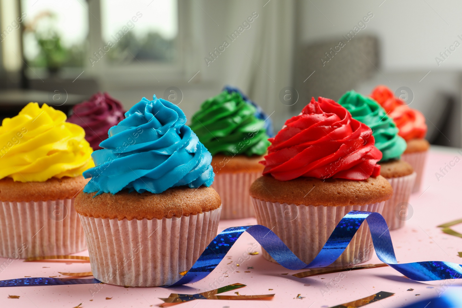 Photo of Many delicious colorful cupcakes and confetti on pink table indoors