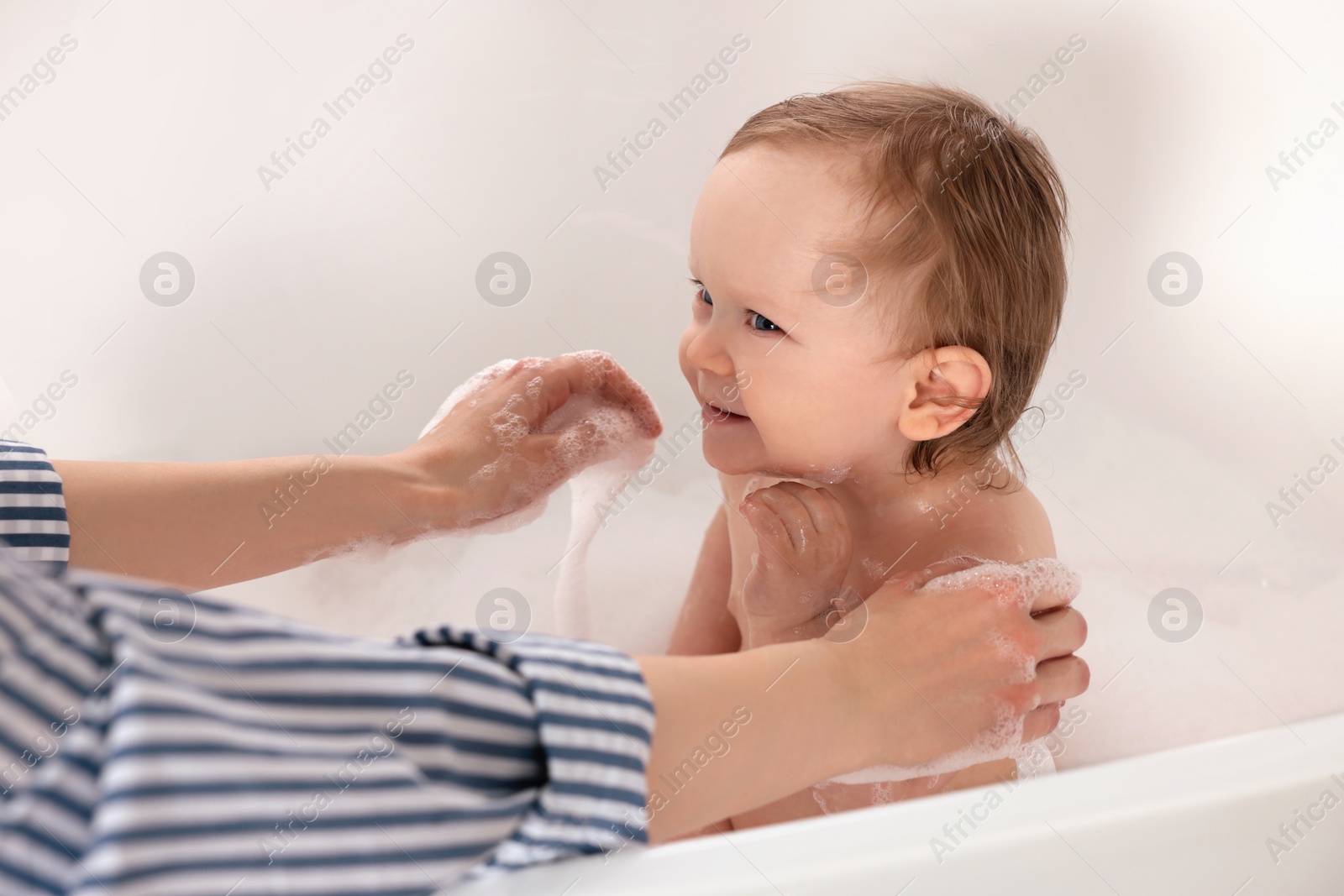 Photo of Mother washing her little baby in tub at home, closeup