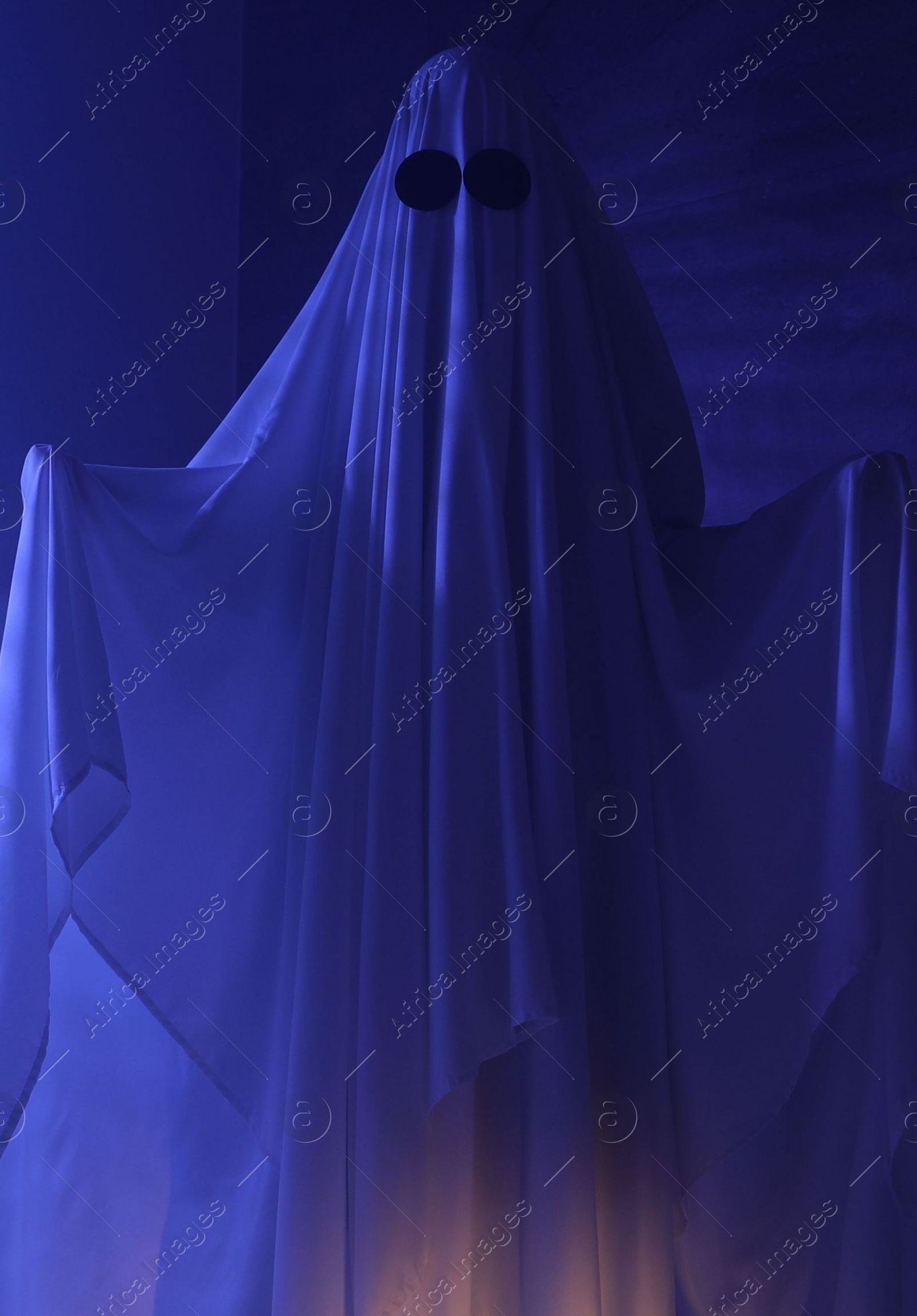 Photo of Creepy ghost. Woman covered with sheet in blue light