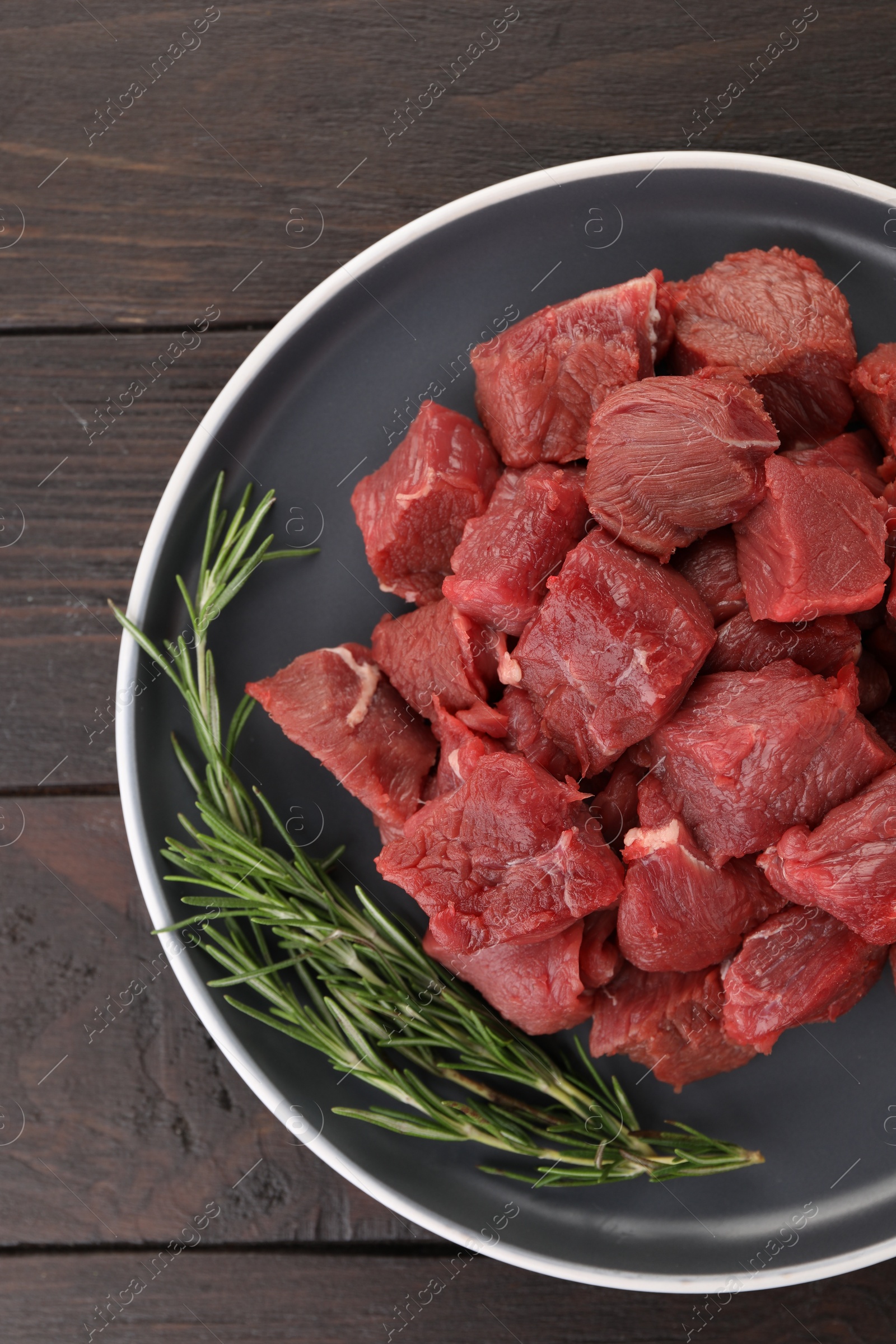 Photo of Pieces of raw beef meat with rosemary on wooden table, top view