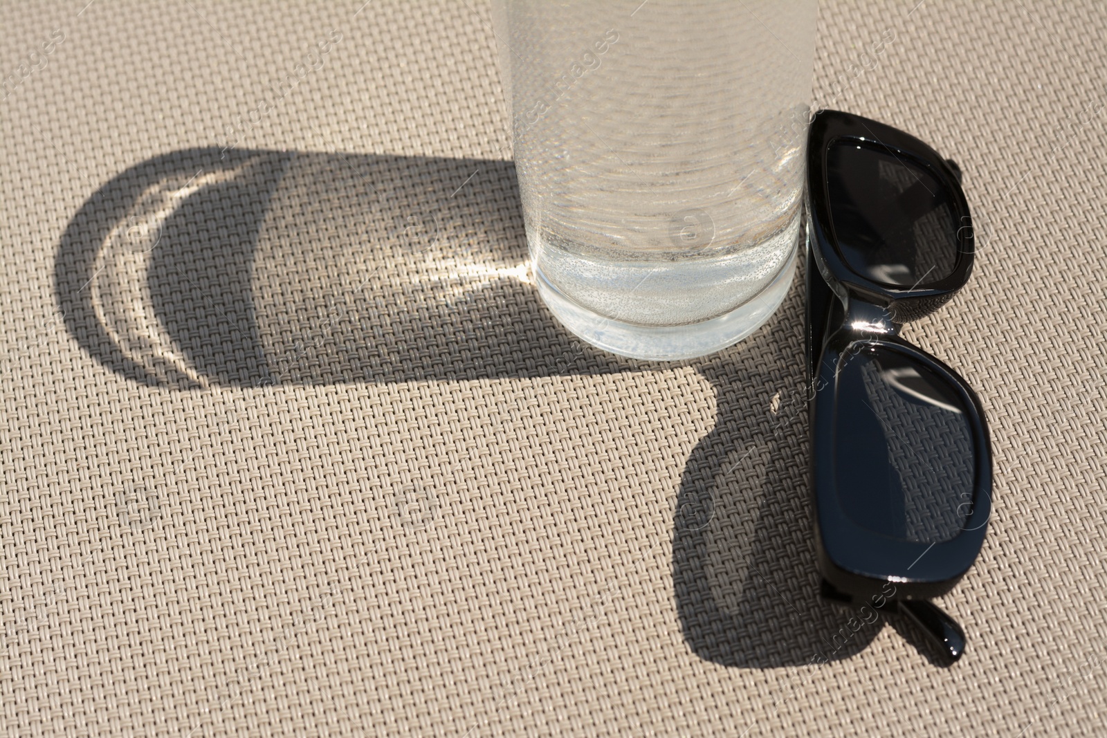Photo of Stylish sunglasses and glass of water on grey surface