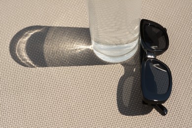 Stylish sunglasses and glass of water on grey surface