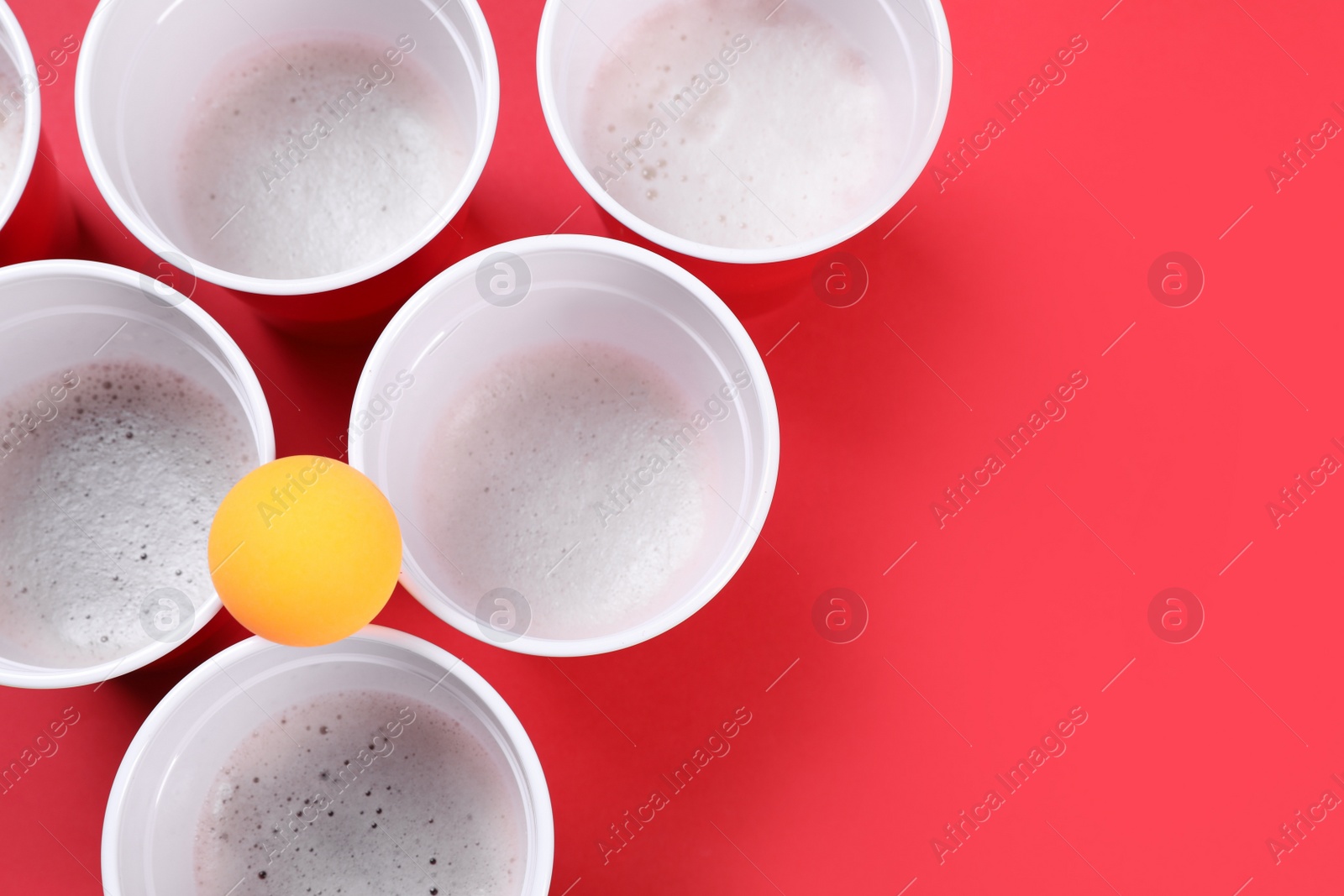 Photo of Plastic cups and ball on red background, flat lay with space for text. Beer pong game