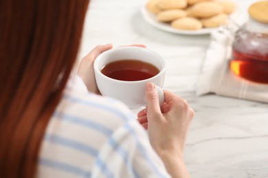Woman with red dyed hair holding cup of tea at white table, closeup