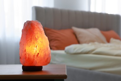 Photo of Himalayan salt lamp on wooden table in bedroom, space for text