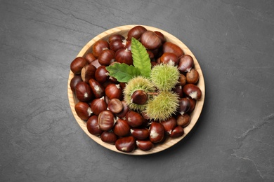 Photo of Fresh sweet edible chestnuts on black slate table, top view