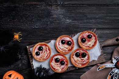 Photo of Cute monster tartlets served on black wooden table, flat lay with space for text. Halloween party food