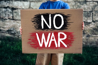 Photo of Boy holding poster with words No War against brick wall outdoors, closeup