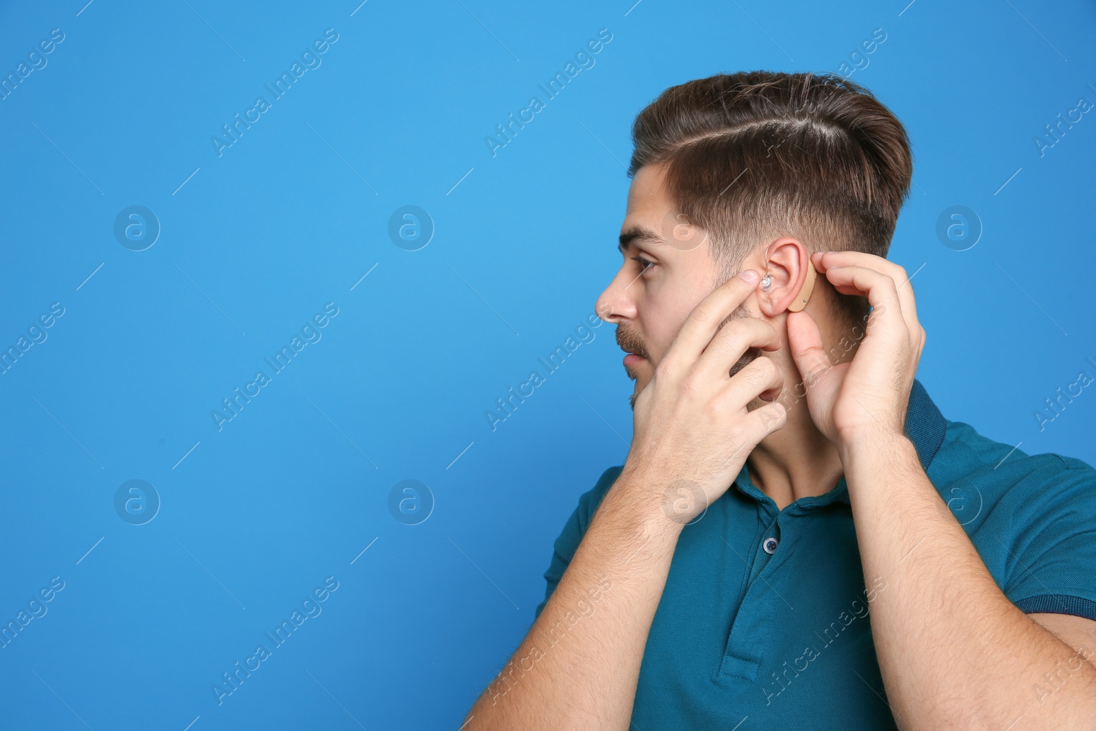 Photo of Young man adjusting hearing aid on color background. Space for text