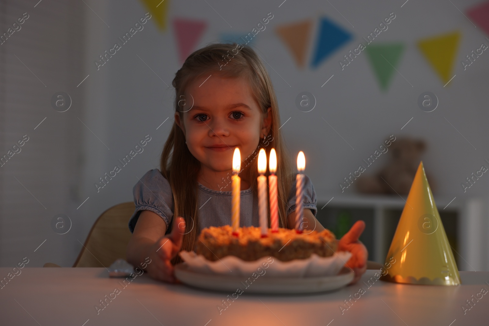 Photo of Cute girl with birthday cake at table indoors