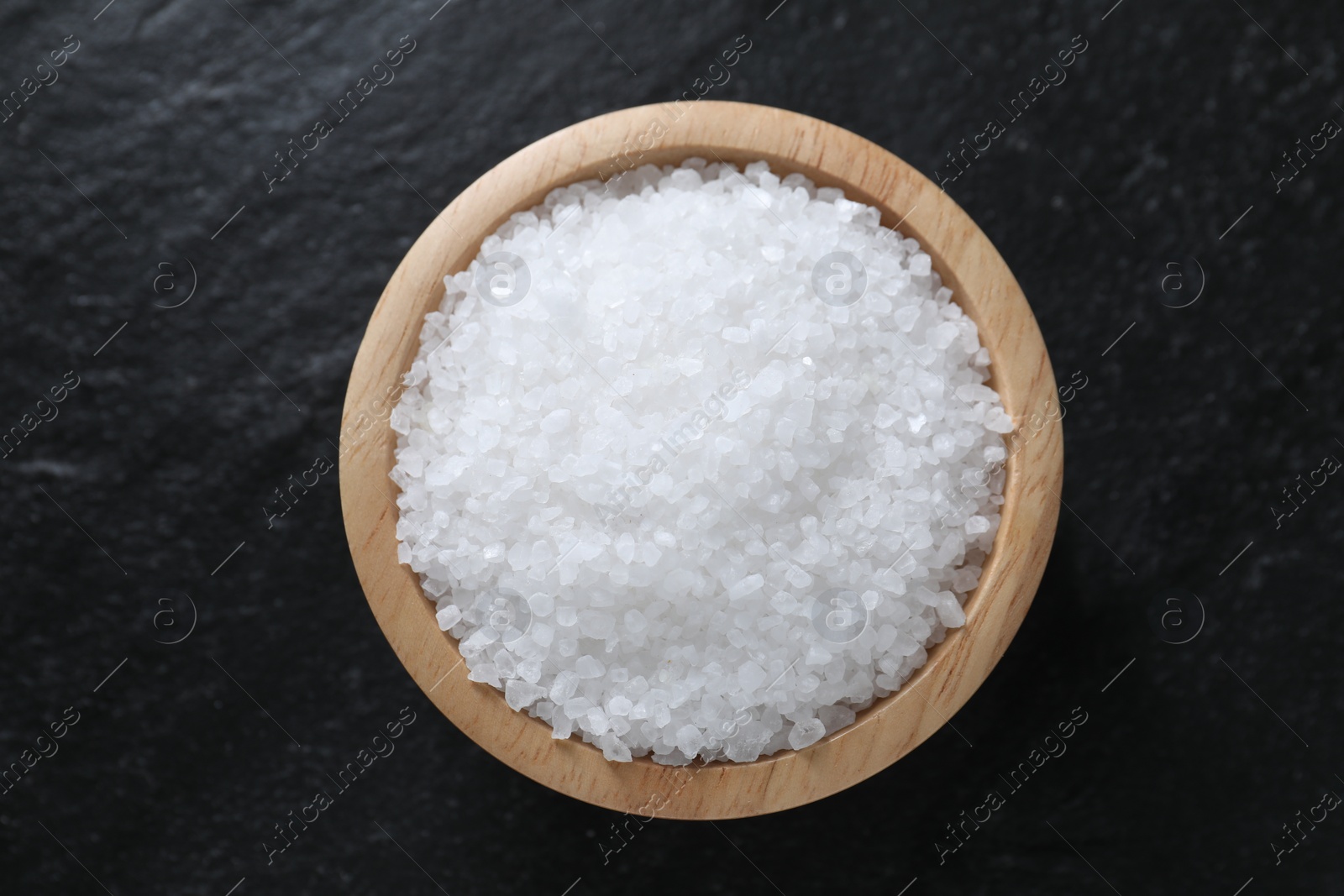 Photo of Organic white salt in bowl on black table, top view