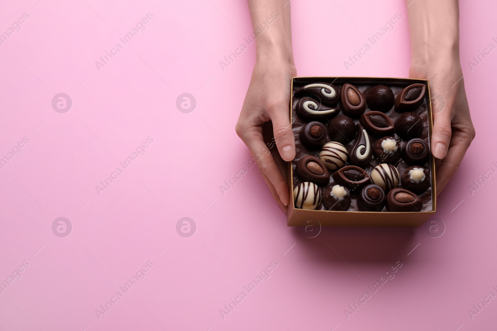 Photo of Woman with box of delicious chocolate candies on pink background, top view. Space for text