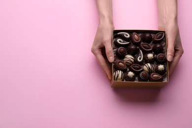 Woman with box of delicious chocolate candies on pink background, top view. Space for text