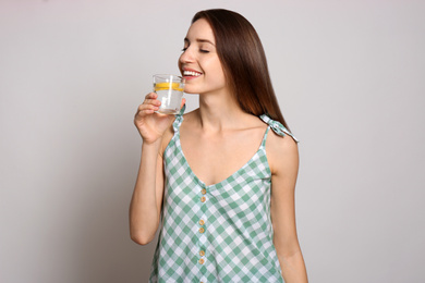 Photo of Young woman drinking lemon water on light background