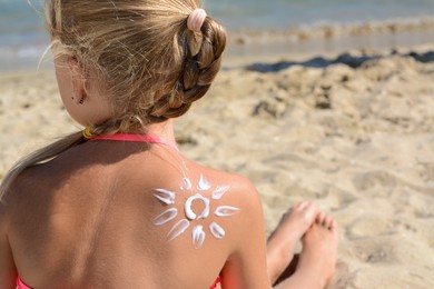 Photo of Little girl with sun protection cream on back near sea, closeup. Space for text
