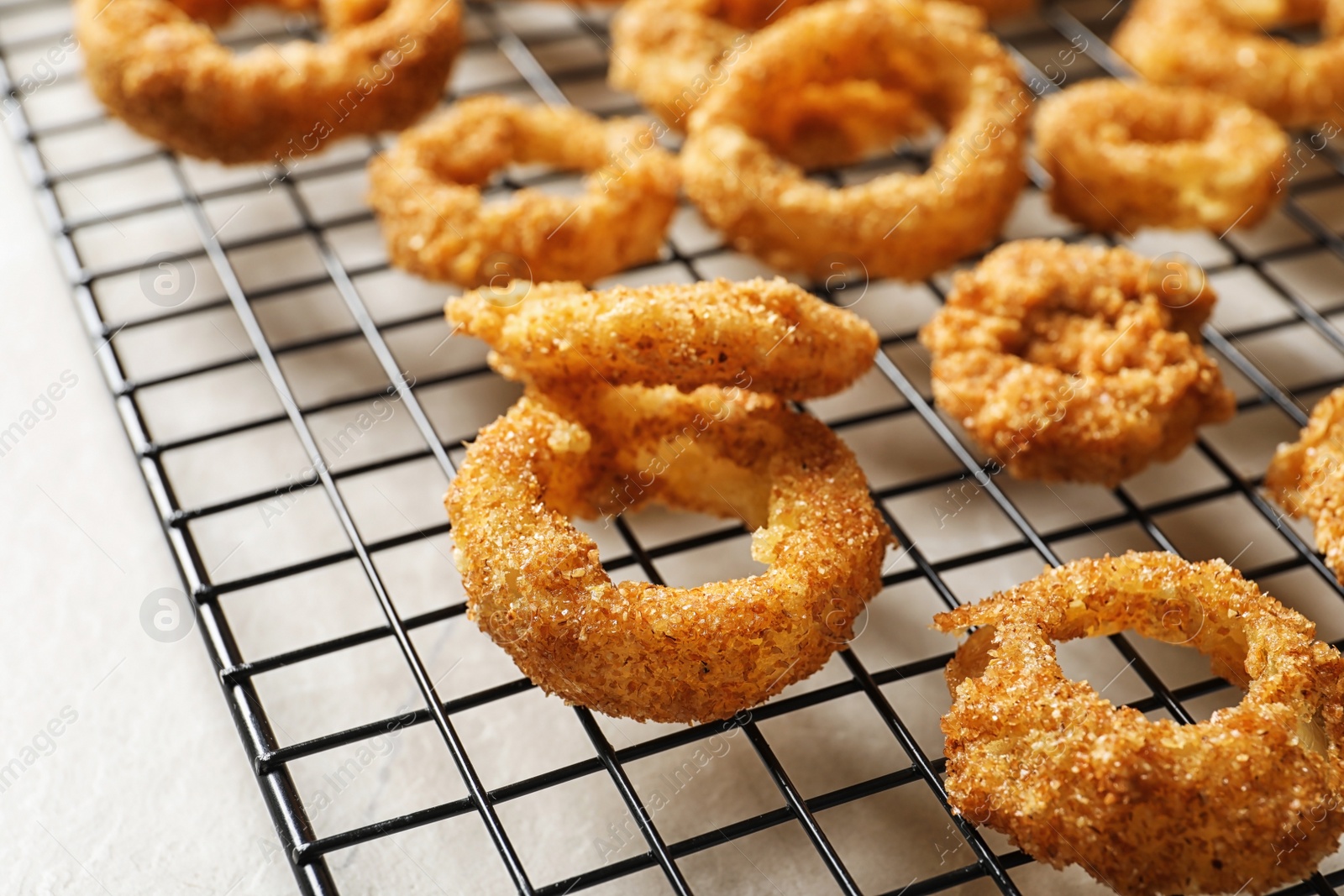 Photo of Cooling rack with homemade crunchy fried onion rings on table, closeup