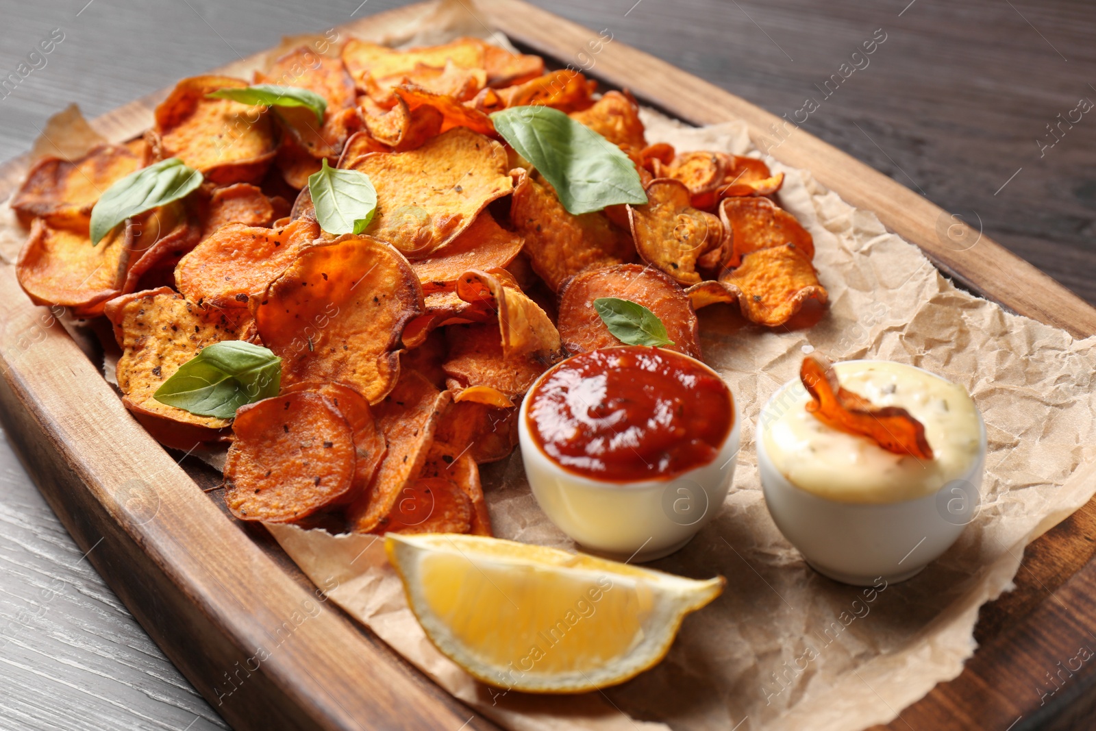 Photo of Tray with sweet potato chips and sauce on wooden table, closeup