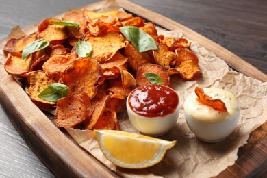 Tray with sweet potato chips and sauce on wooden table, closeup