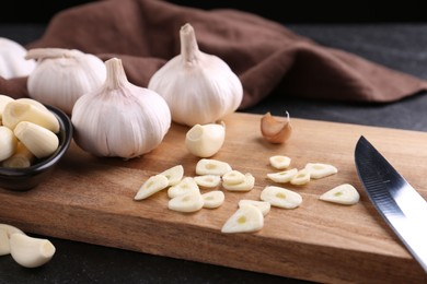 Photo of Aromatic cut garlic, cloves and bulbs on dark table, closeup