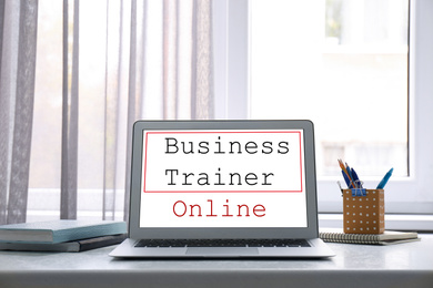 Image of Modern laptop with text BUSINESS TRAINER ONLINE on table indoors