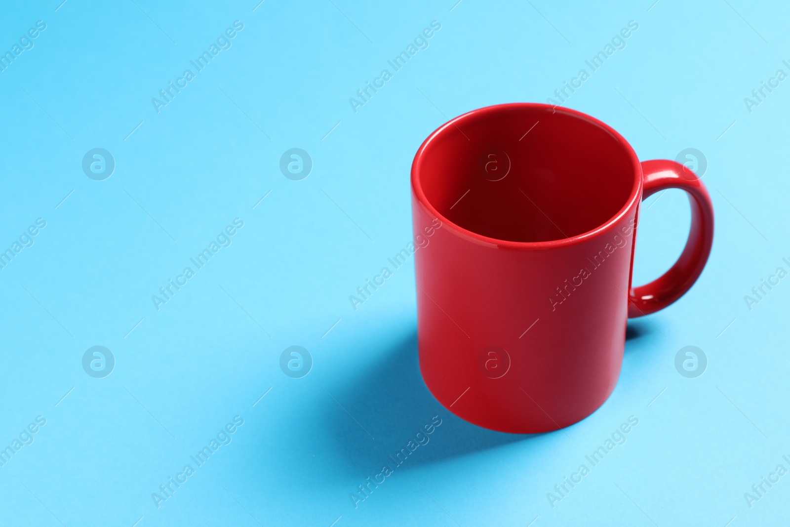 One red ceramic mug on light blue background, space for text Photo of One red ceramic mug on light blue background, space for text