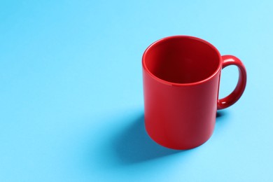 Photo of One red ceramic mug on light blue background, space for text