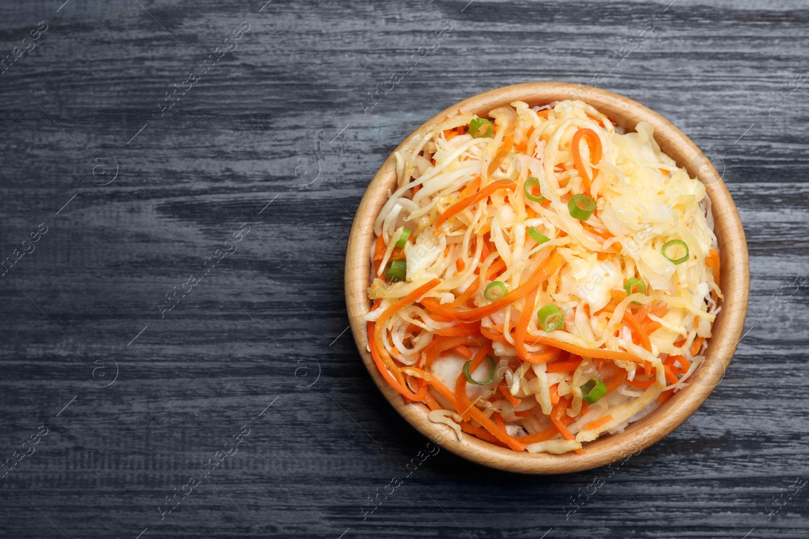 Photo of Tasty fermented cabbage with carrot on black wooden table, top view. Space for text