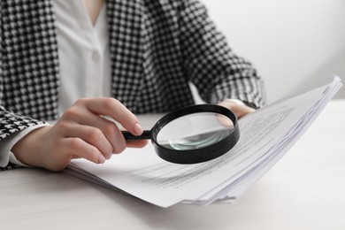 Woman looking at document through magnifier at white wooden table, closeup. Searching concept