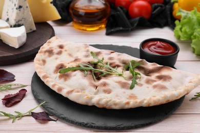 Delicious calzone and products on light wooden table, closeup