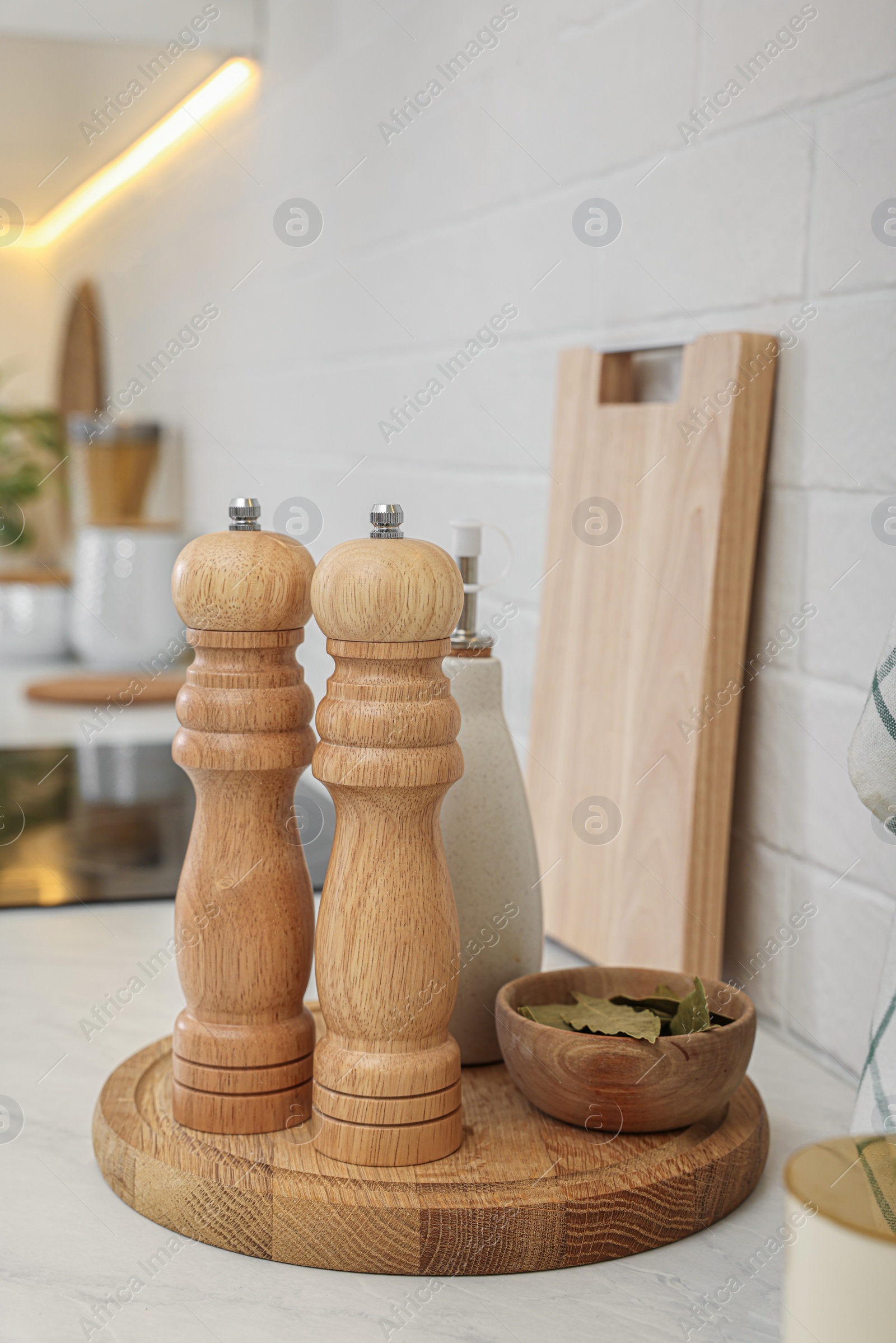 Photo of Wooden salt and pepper shakers, bowl with bay leaves on white countertop in kitchen