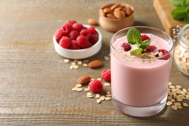 Photo of Glass of tasty raspberry smoothie with oatmeal and mint on wooden table, space for text