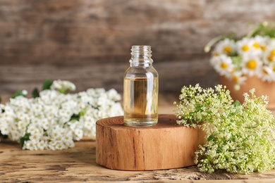 Bottle of essential oil with flowers on wooden table, space for text