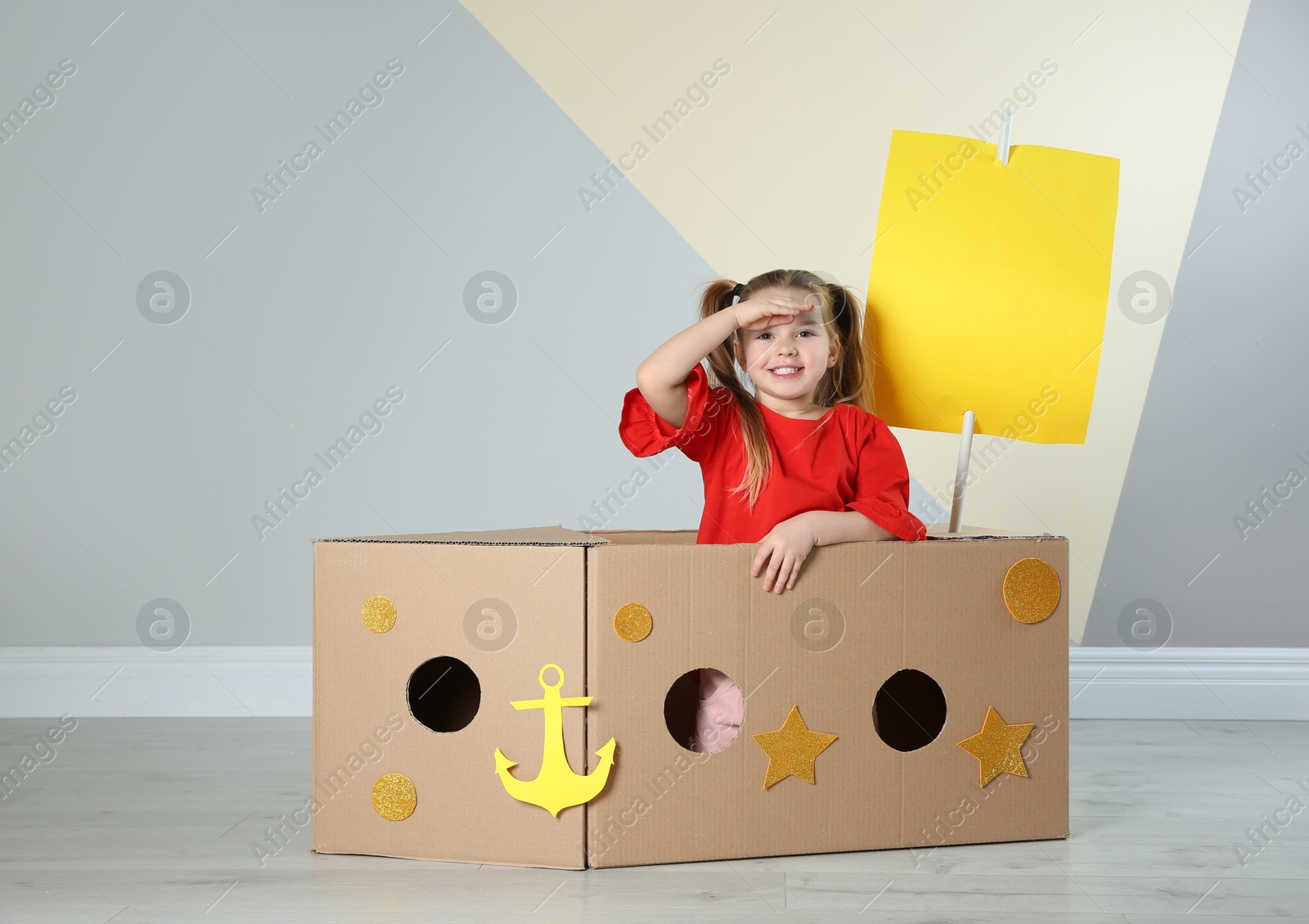 Photo of Cute little child playing with cardboard ship near color wall