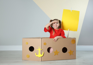 Cute little child playing with cardboard ship near color wall