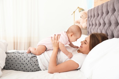 Photo of Young mother playing with her cute baby on bed indoors