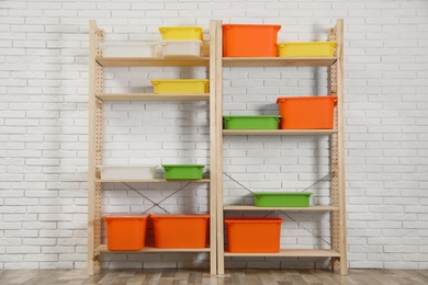 Photo of Wooden shelving units with colorful containers near white brick wall. Stylish room interior