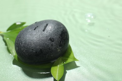 Photo of Spa stone and fresh leaves on light green background, closeup. Space for text